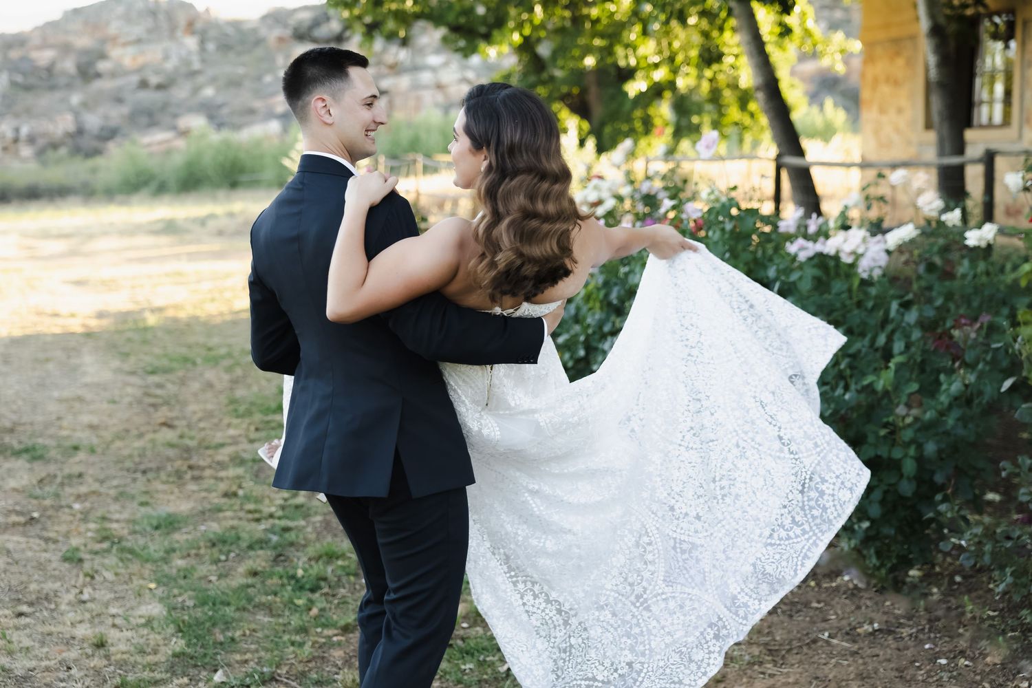 A couple shares an intimate dance moment outdoors while holding a delicate white lace veil in the sunlight.
