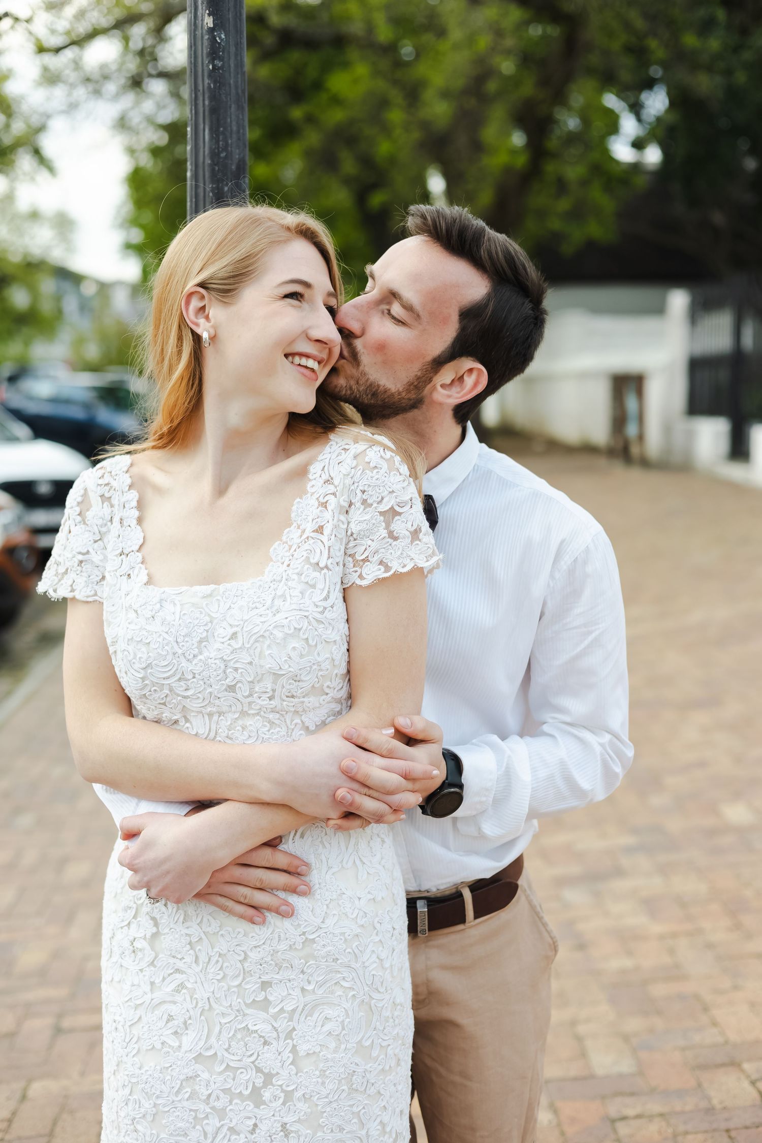 A couple in wedding attire share intimate moments while dancing together on a brick paved path.