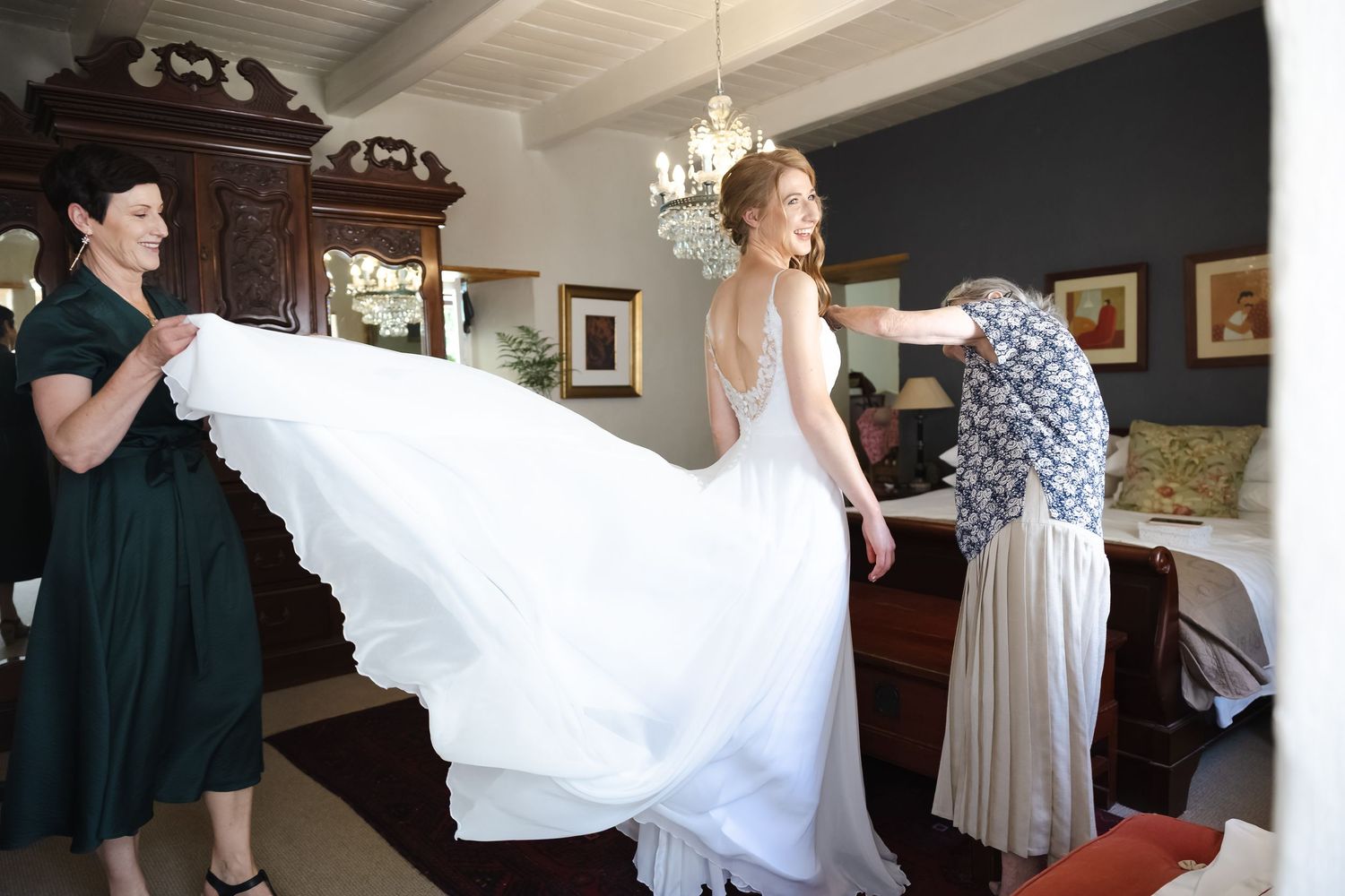 A flowing white wedding dress being lifted and fluffed by helping hands in preparation for a special occasion.