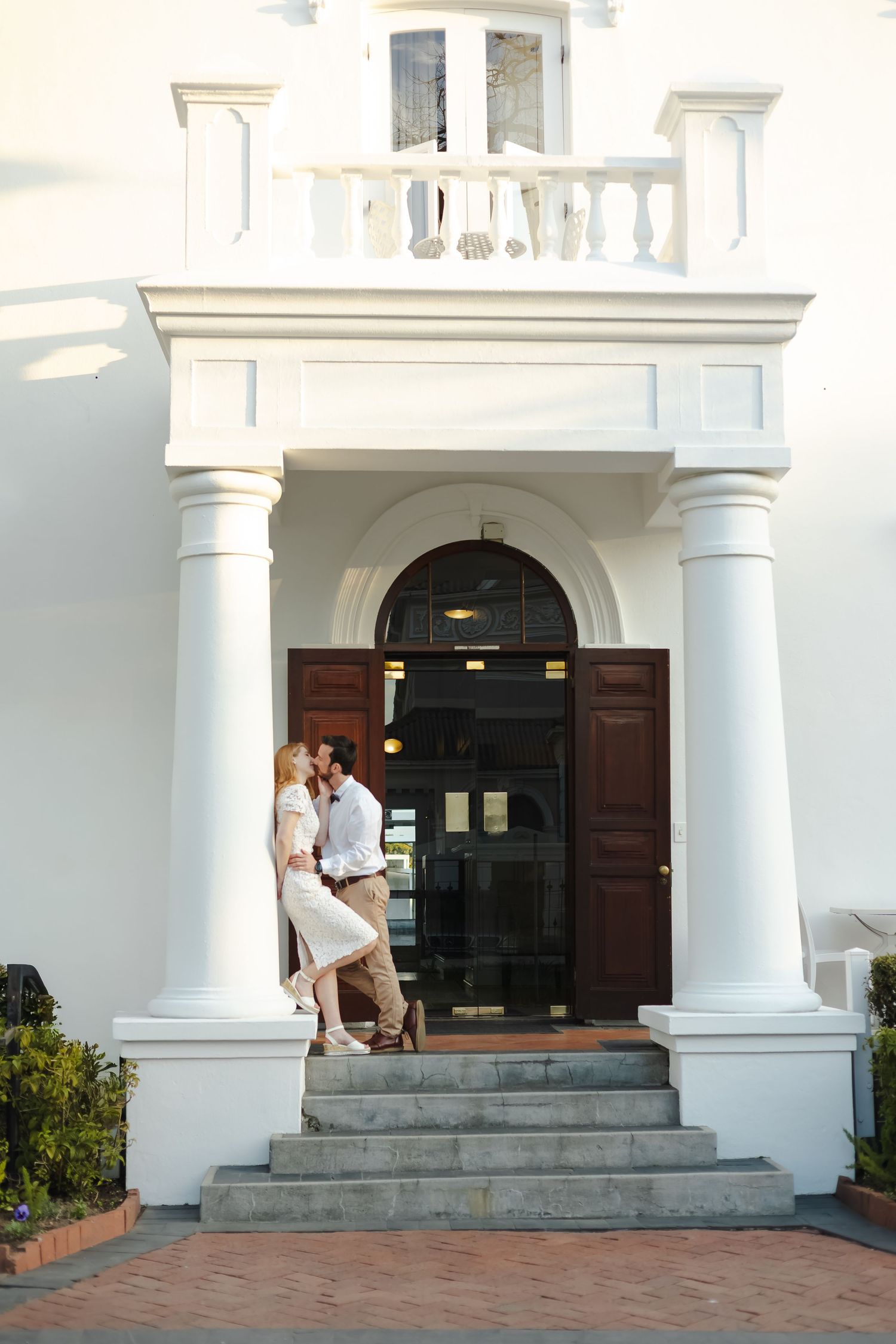 Elegant white colonial entrance with grand columns and stone steps leading to dark wooden double doors.