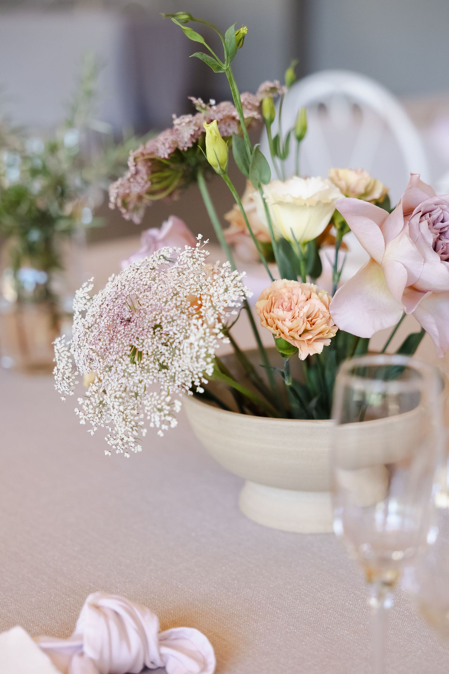 Delicate floral centerpieces featuring soft pink roses and baby's breath in white ceramic bowls on a neutral tablecloth.