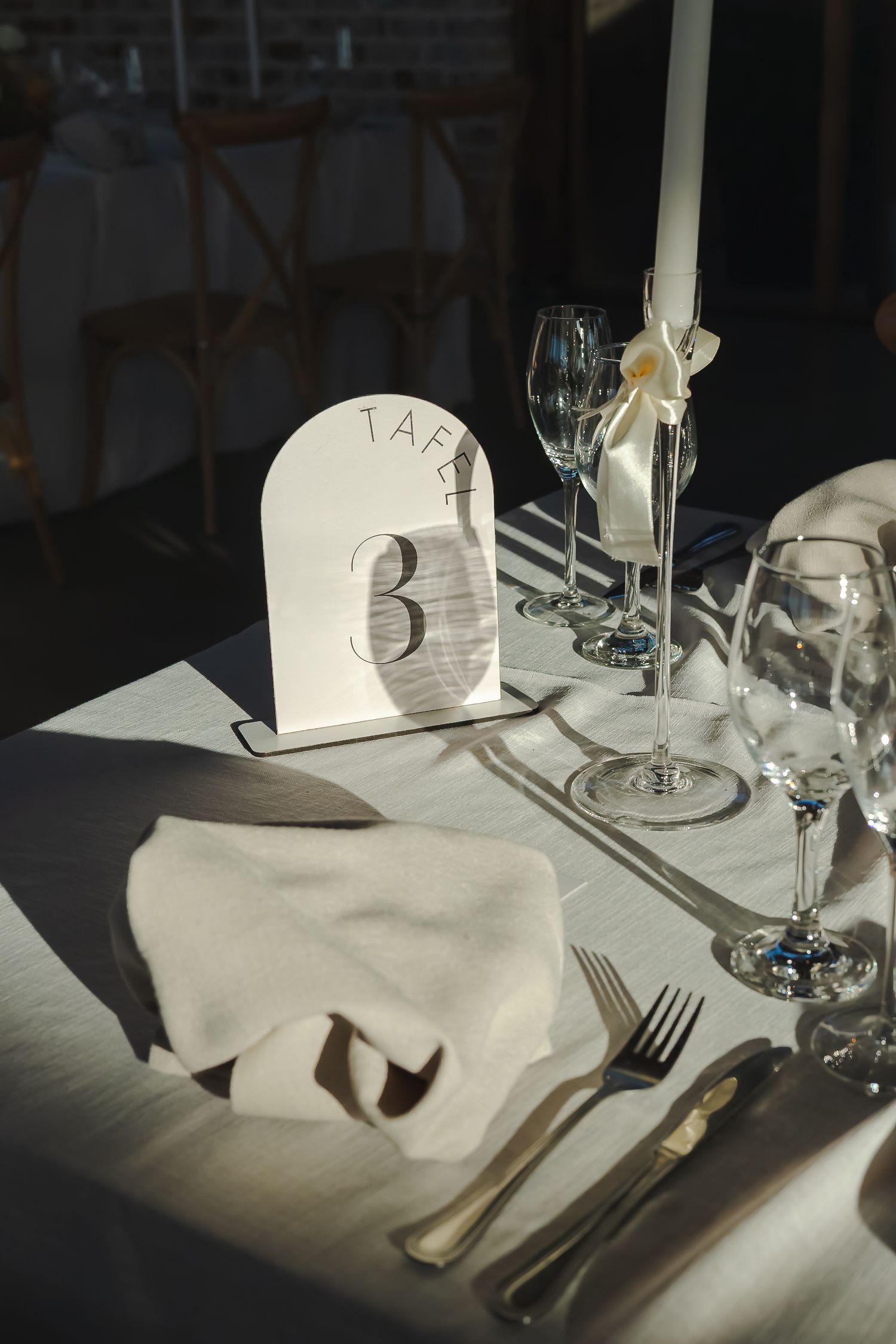 Elegant white table setting with polished silverware and wine glasses arranged on pristine white linens.