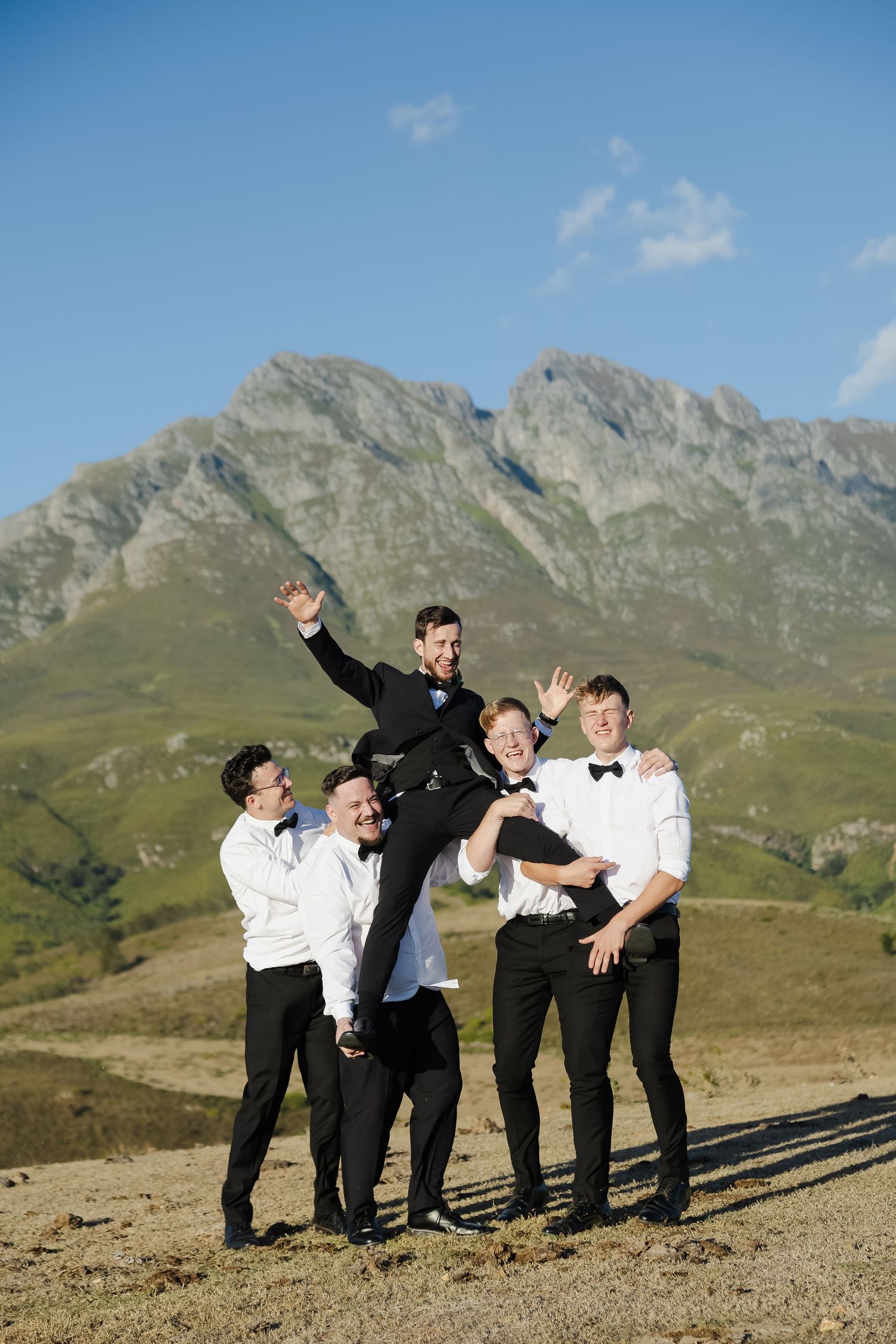 Groomsmen strike dynamic poses in black and white attire against rugged mountain scenery.