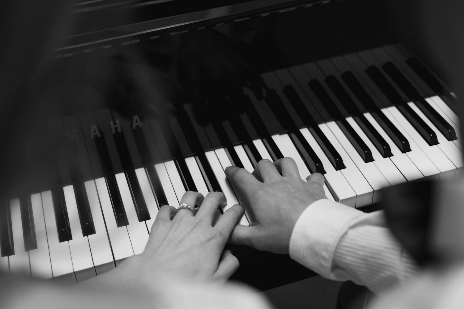Multiple hands playing piano keys in dramatic black and white lighting creating a dynamic musical sequence.