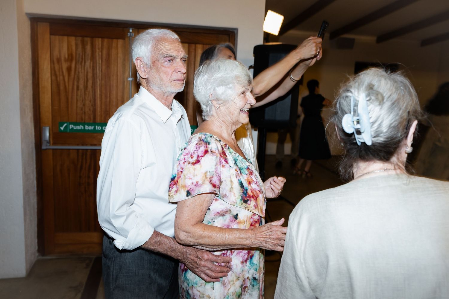 Elderly couples dancing together at a wedding reception in a dimly lit venue.
