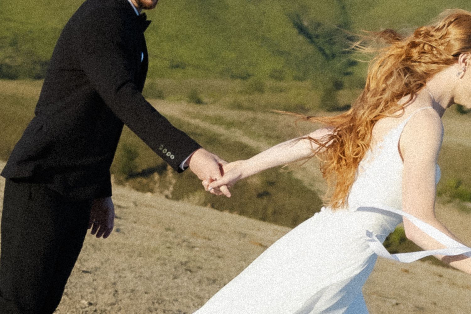 A couple in formal wedding attire dances and spins together on a scenic hillside during their celebration.