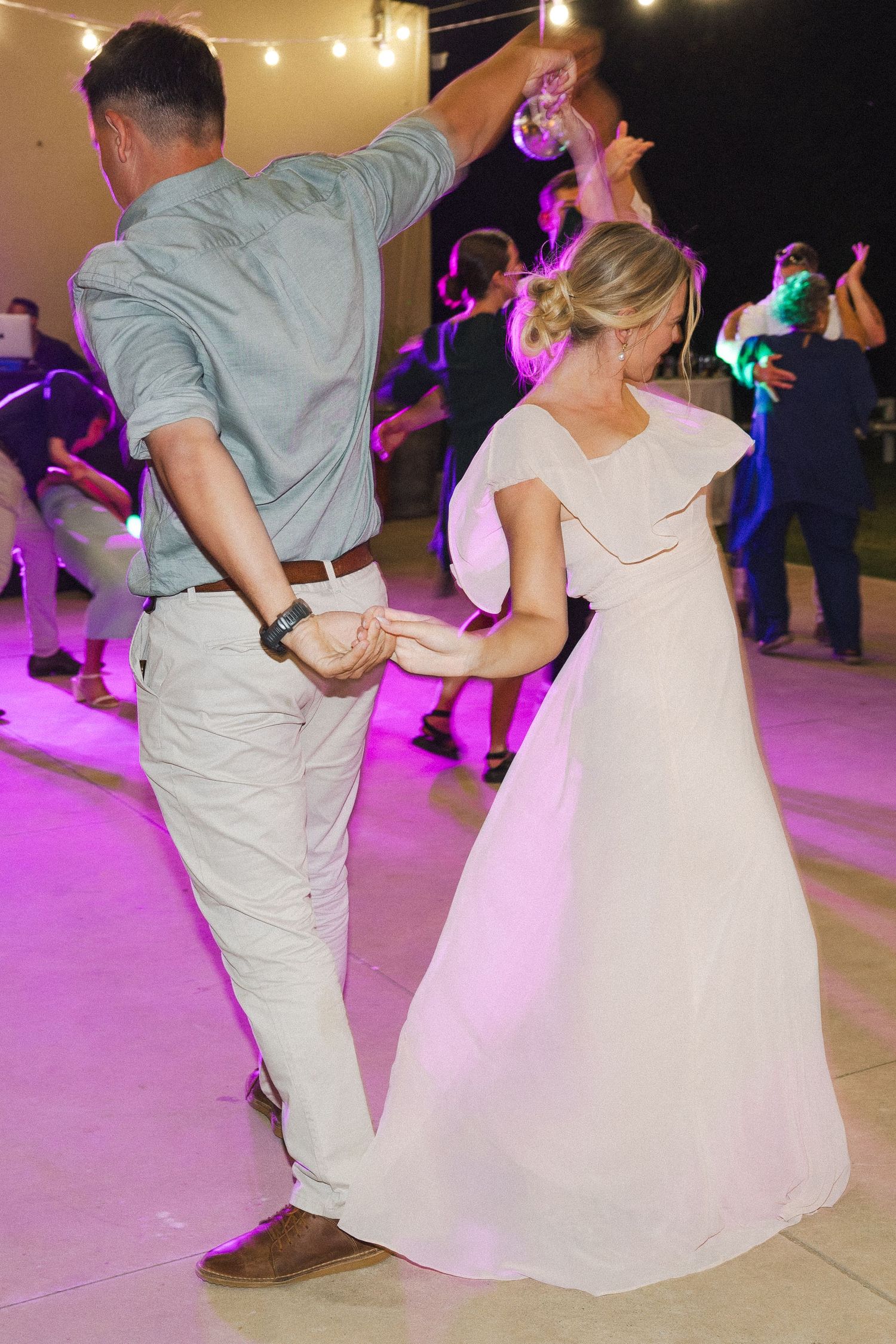 A couple dances together at a wedding reception with purple lighting illuminating the dance floor.