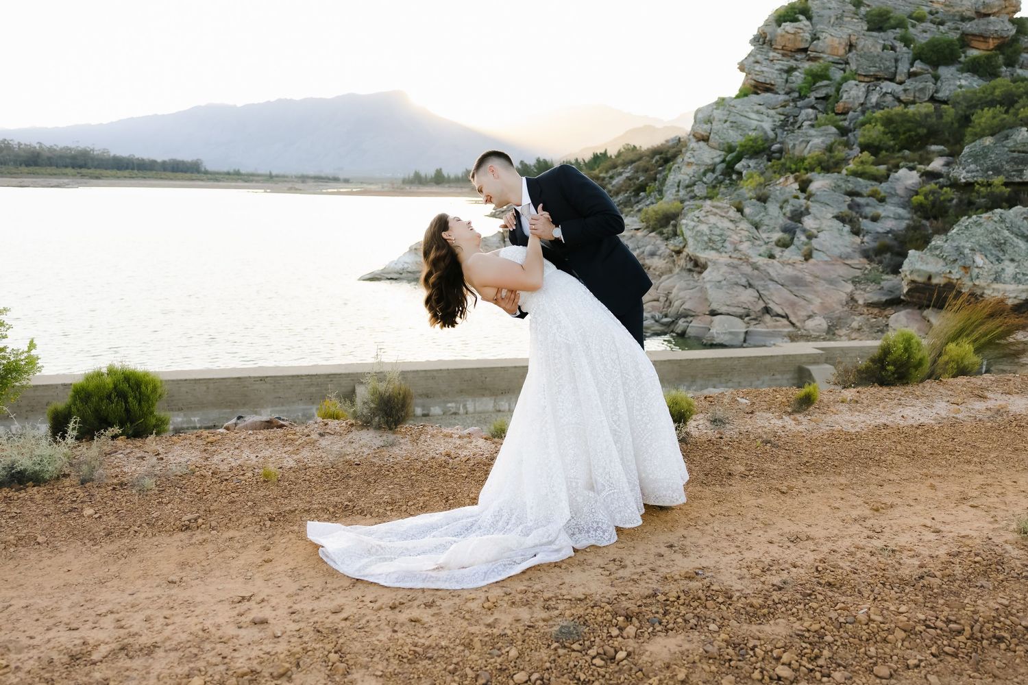 Wedding couple poses against dramatic coastal landscape with mountains and water at golden hour.
