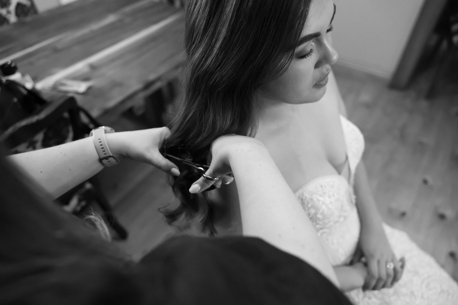 Black and white photo of hairstylist working on bride's hair during wedding preparation.