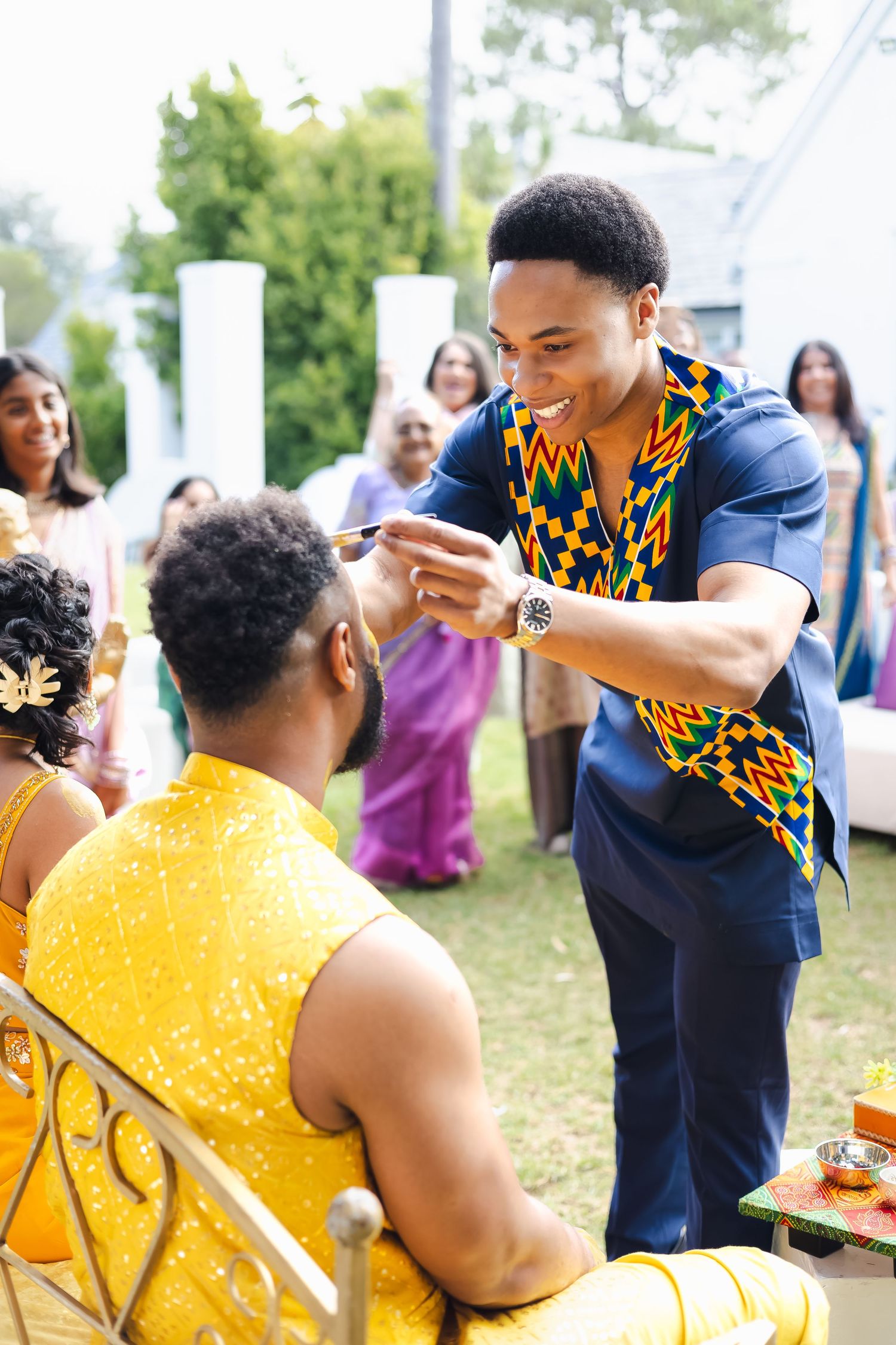 Guests participate in a cultural celebration wearing traditional African prints and formal attire at an outdoor event.