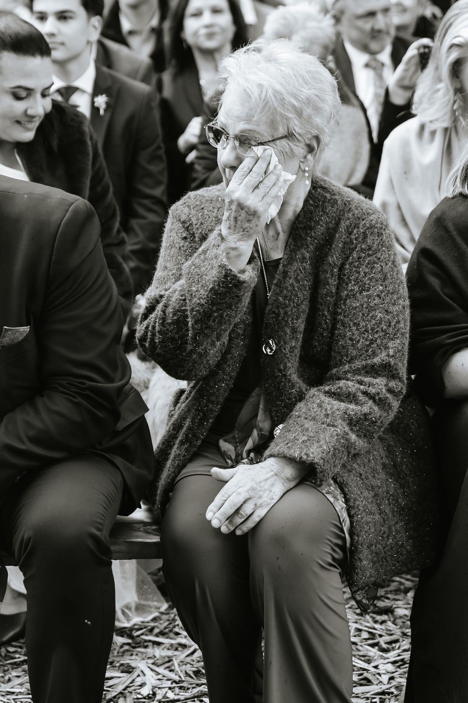 Elderly woman crying with hand over face at outdoor wedding ceremony, black and white photo.