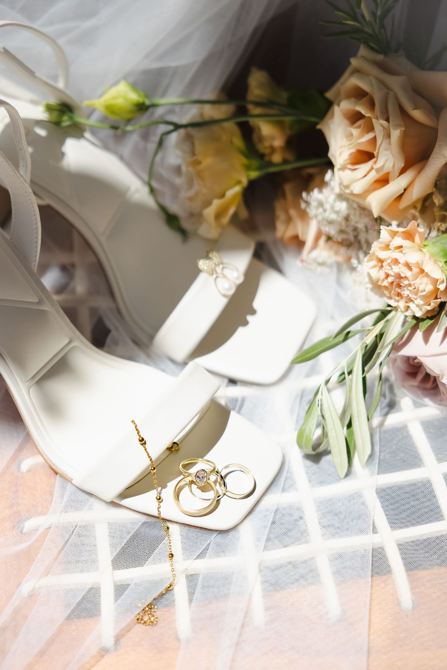 Wedding details featuring delicate floral arrangements and rings displayed on white paper in soft natural light.