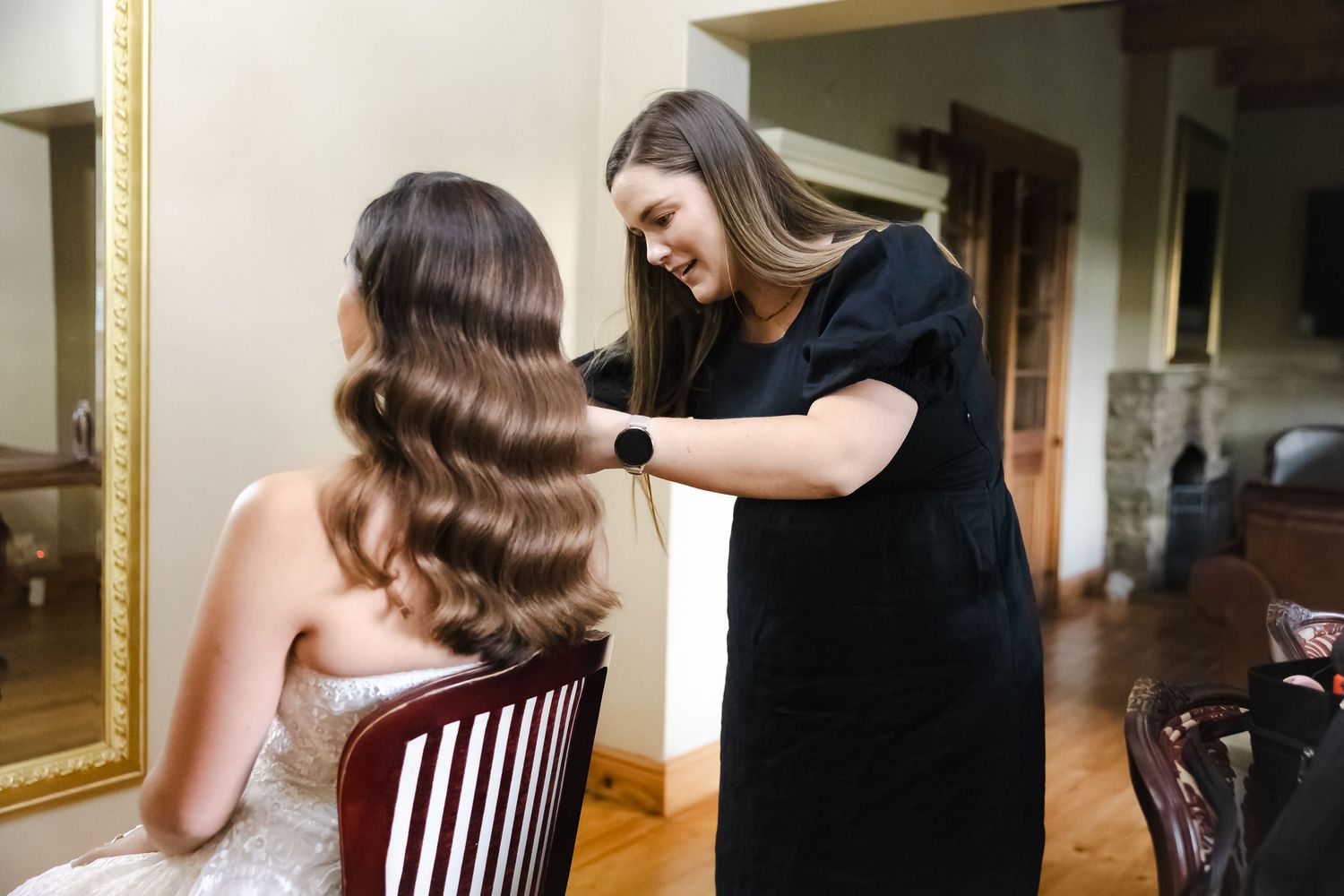 A stylist works on a client's elegant vintage-inspired hairstyle in a salon setting.