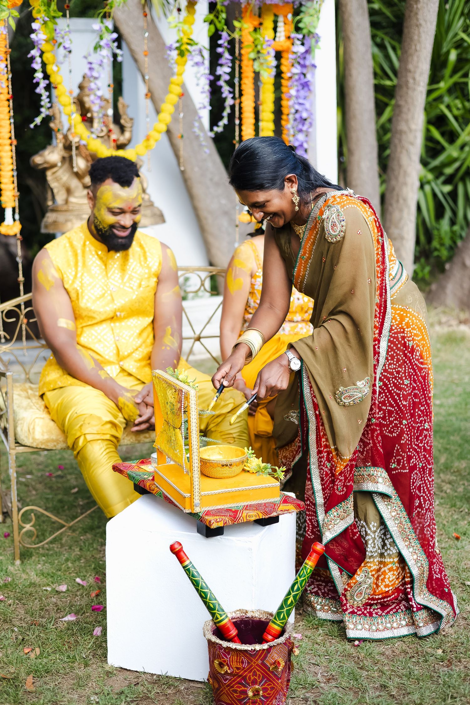 Traditional Indian wedding ceremony details showing decorative elements in yellow and red with floral arrangements outdoors.
