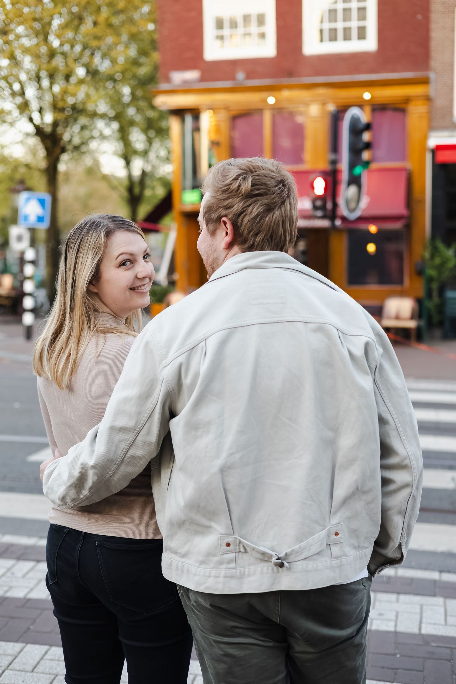 A couple walks together on a city street, the woman smiling at her partner near a crosswalk.