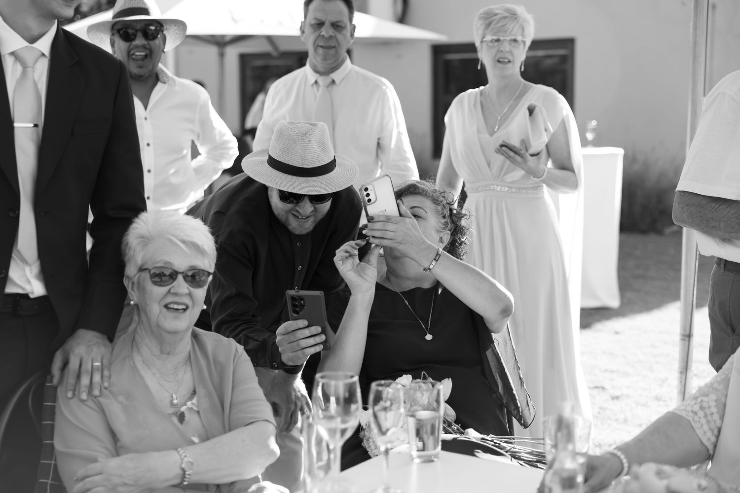 A black and white photo of people gathered at an outdoor event with wine glasses and drinks.