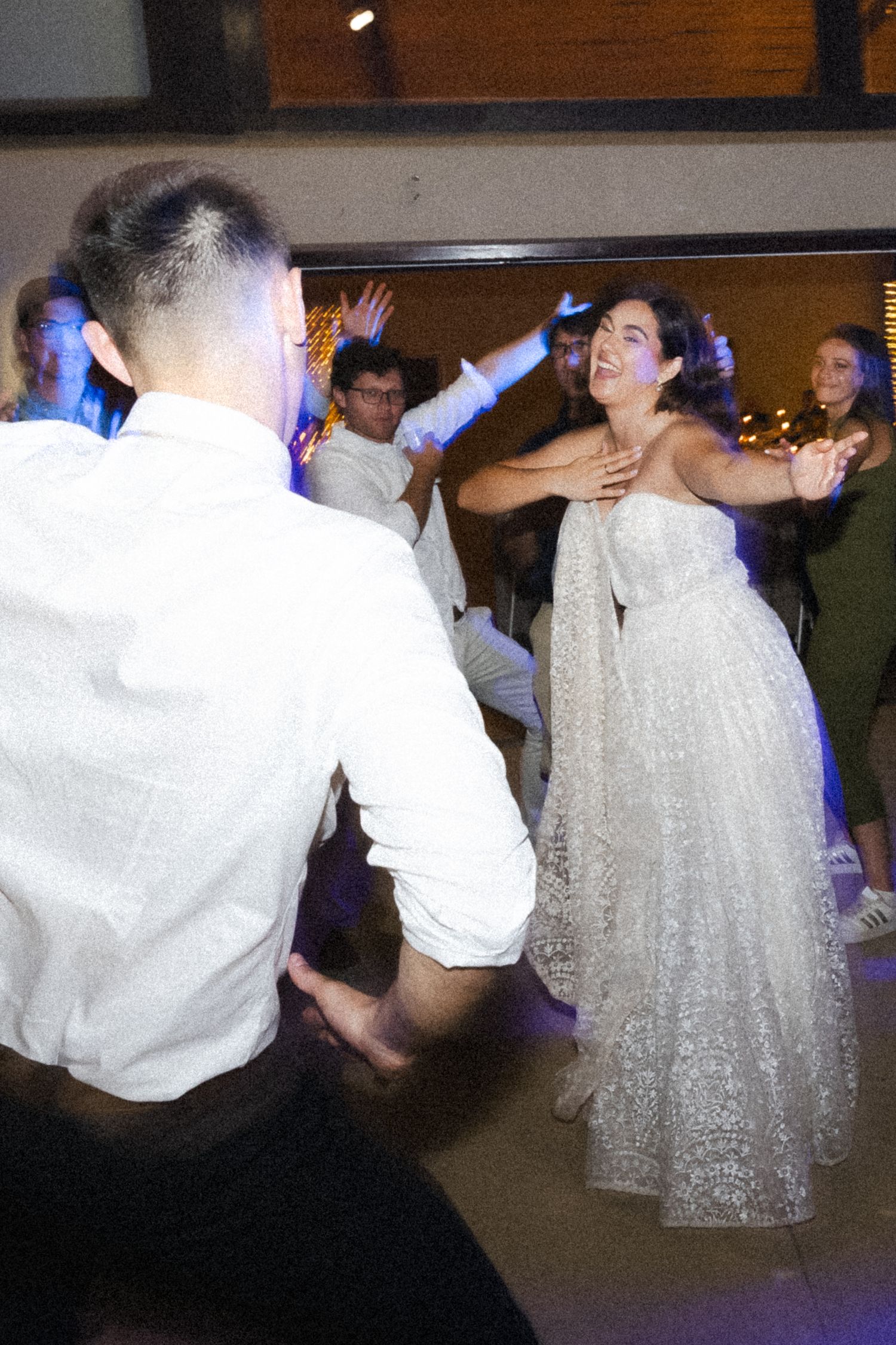 A couple dancing energetically at a wedding reception, with the bride wearing a sparkly white dress.