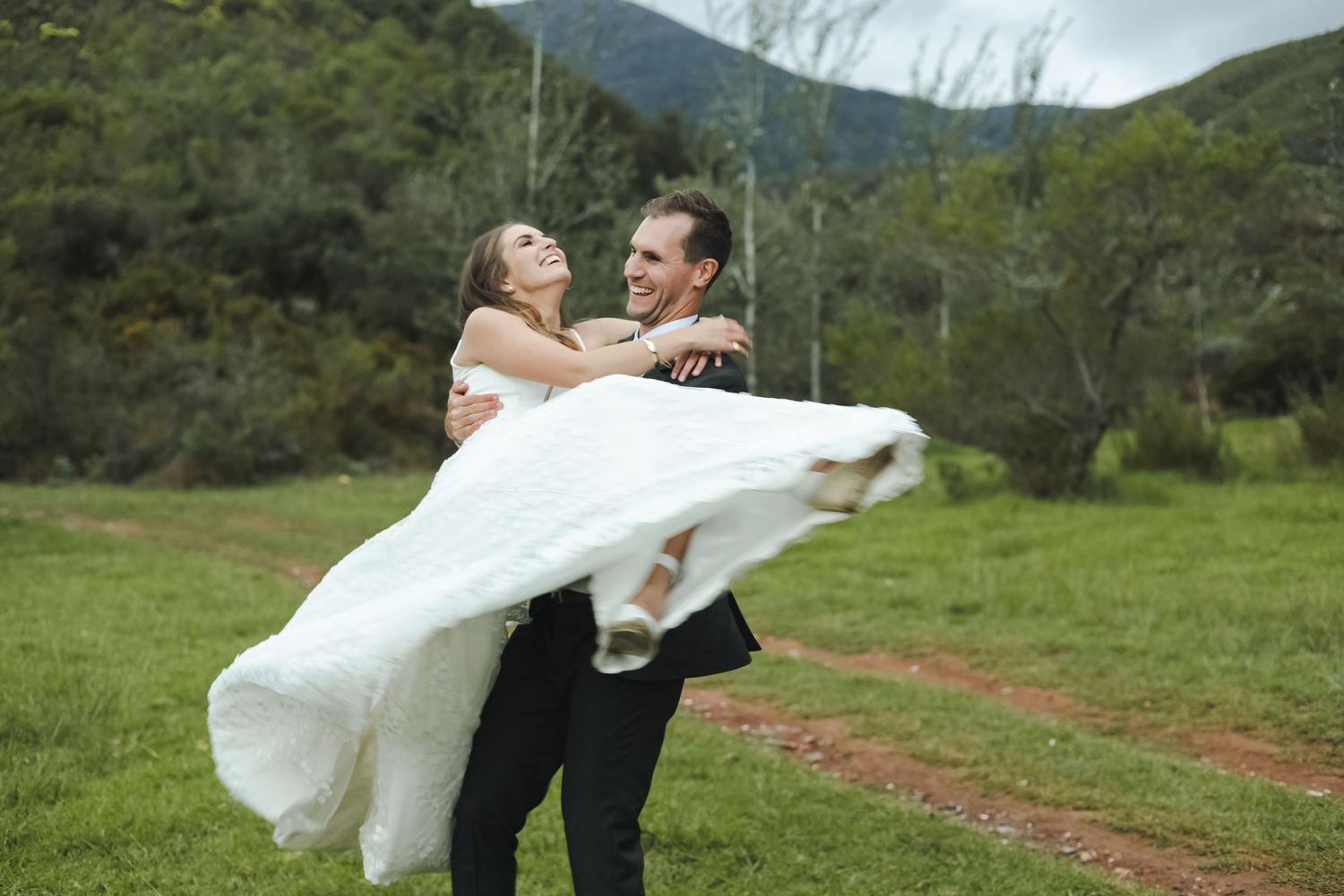 Couple celebrates with playful poses in a green mountain meadow.