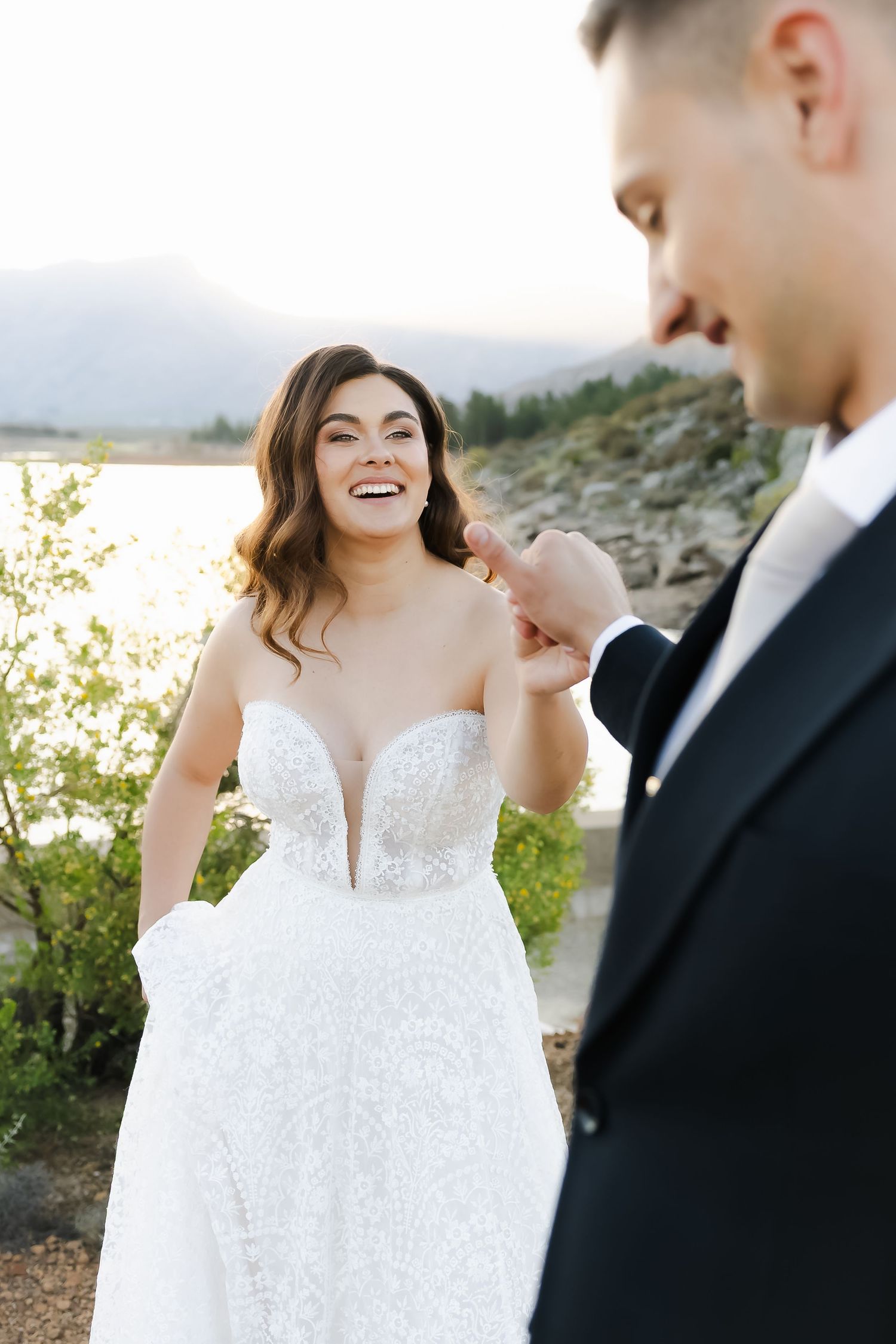 Bride in white lace dress twirls joyfully during sunset photoshoot.
