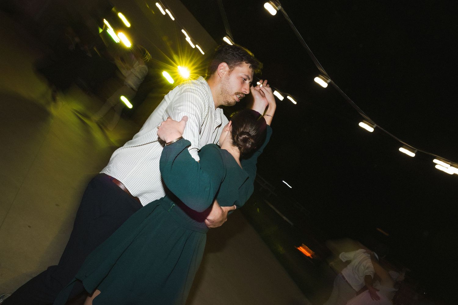 A couple in formal attire dance together at a dimly lit wedding reception with dramatic lighting effects.