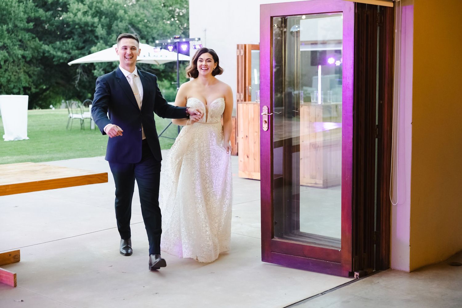 A couple exits through a glass door at an event venue with purple and orange interior decor.
