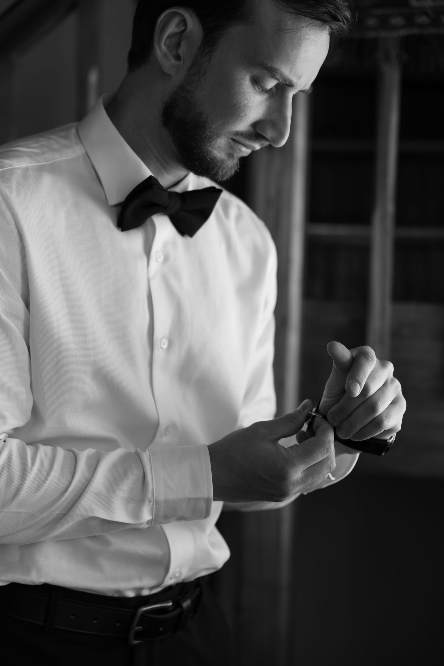 Person in formal attire adjusts their bow tie while getting dressed in black and white.