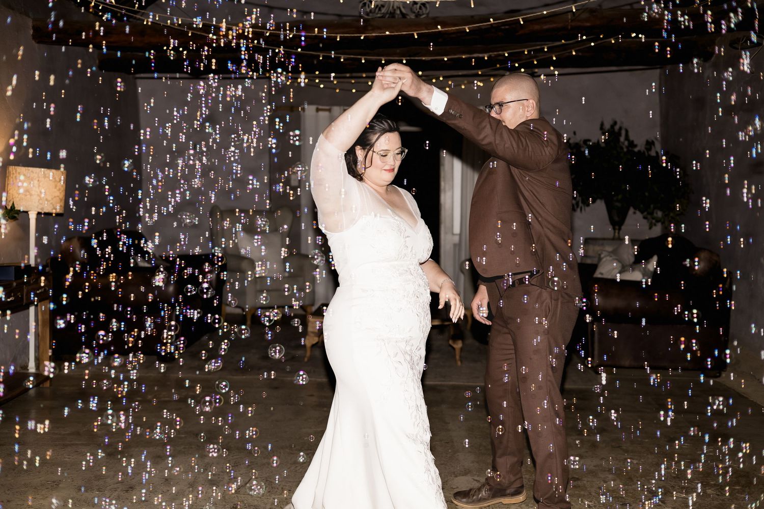Bride and groom share first dance surrounded by floating bubbles at elegant wedding reception.