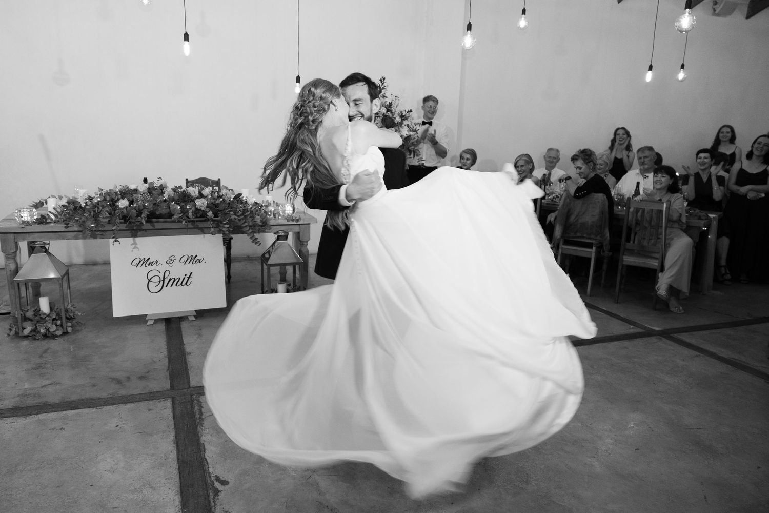 A couple performs a graceful dance move in a ballroom with guests watching from the sides during a wedding celebration.
