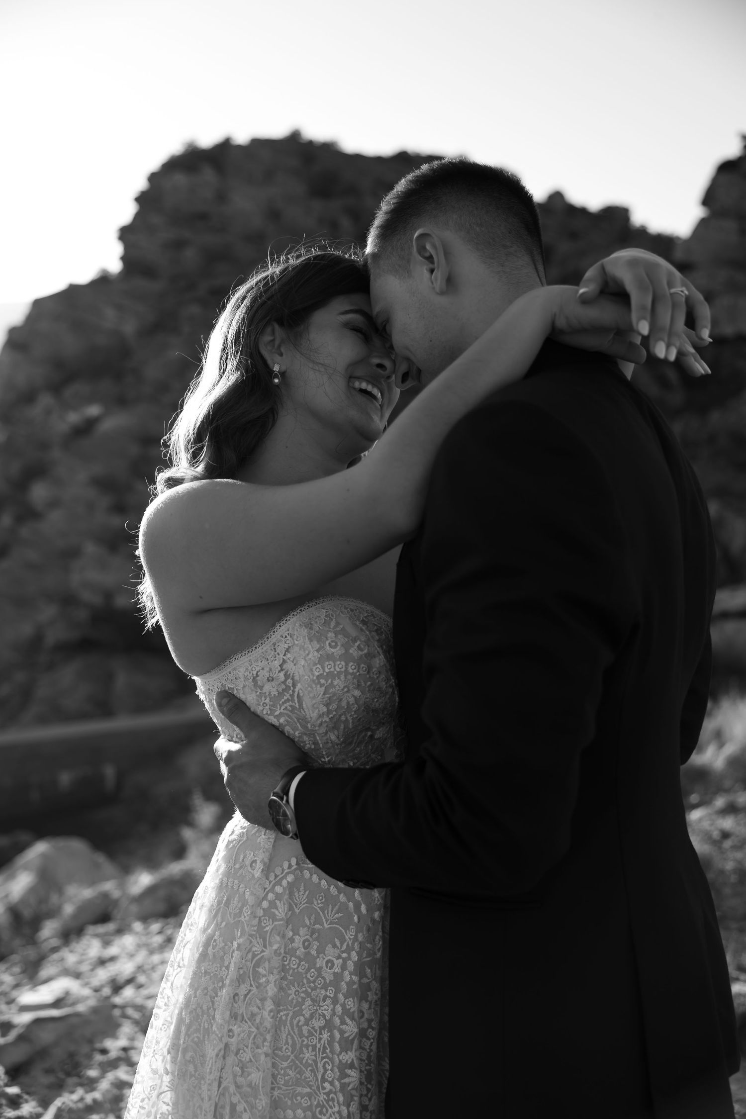 A romantic black and white wedding photo of a couple embracing against a rocky mountain backdrop.