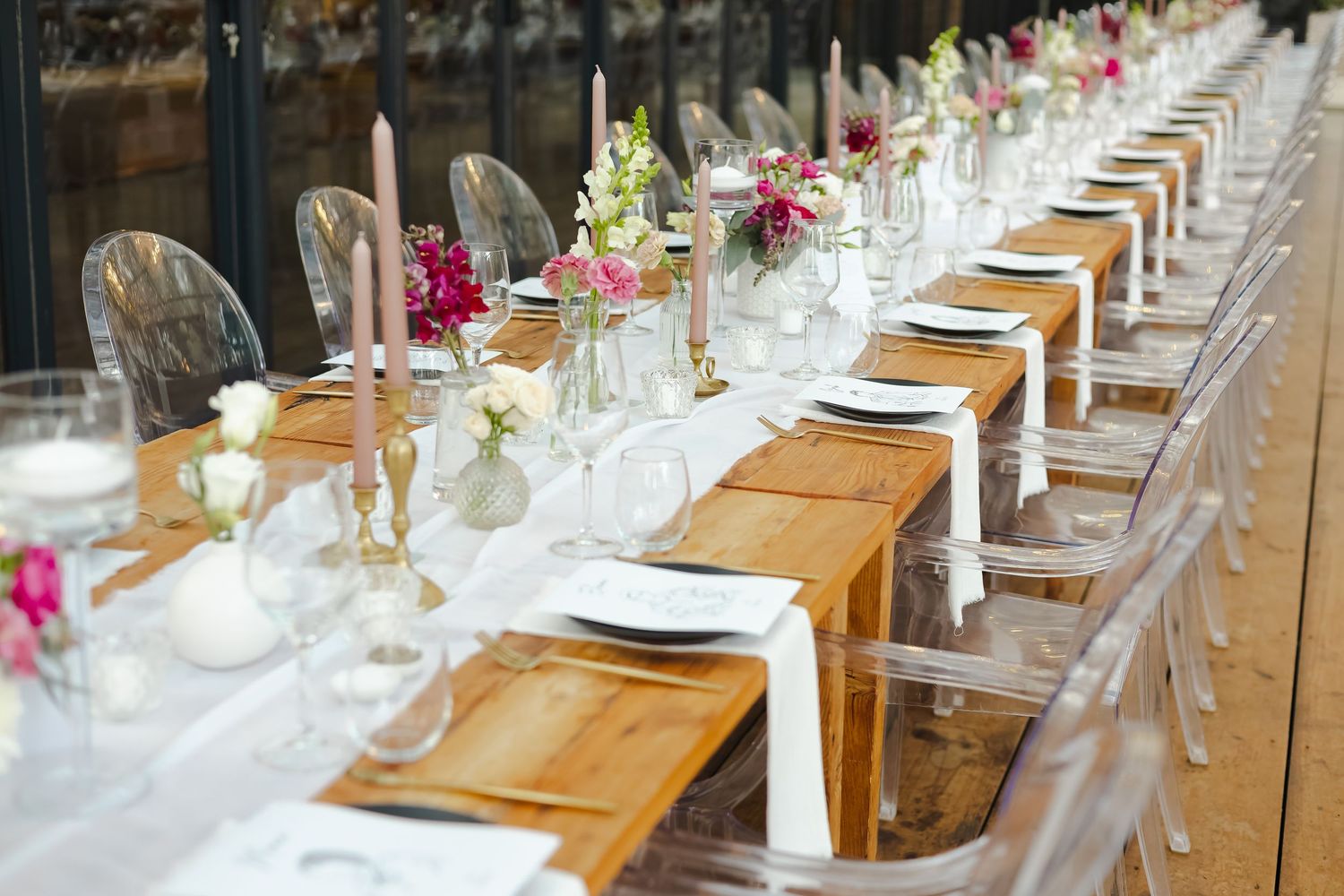 Long rustic dining tables set with elegant place settings and floral arrangements for wedding reception.