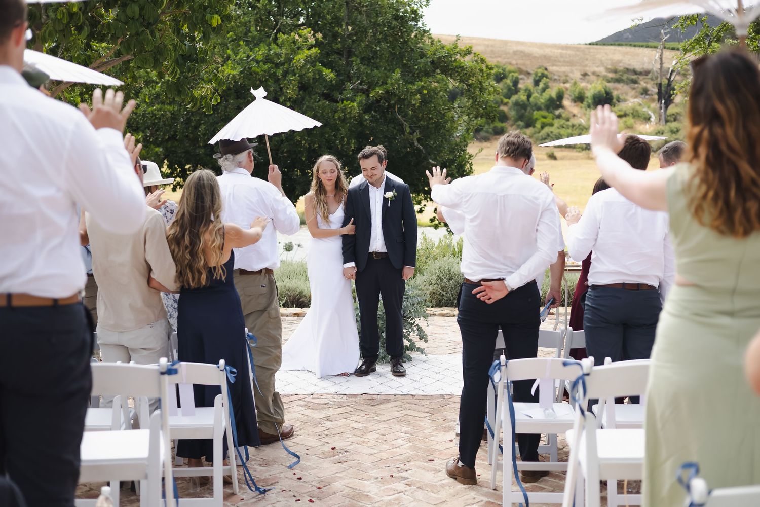 Wedding guests mingle and dance at an outdoor reception venue with white chairs and scenic mountain views in the background.
