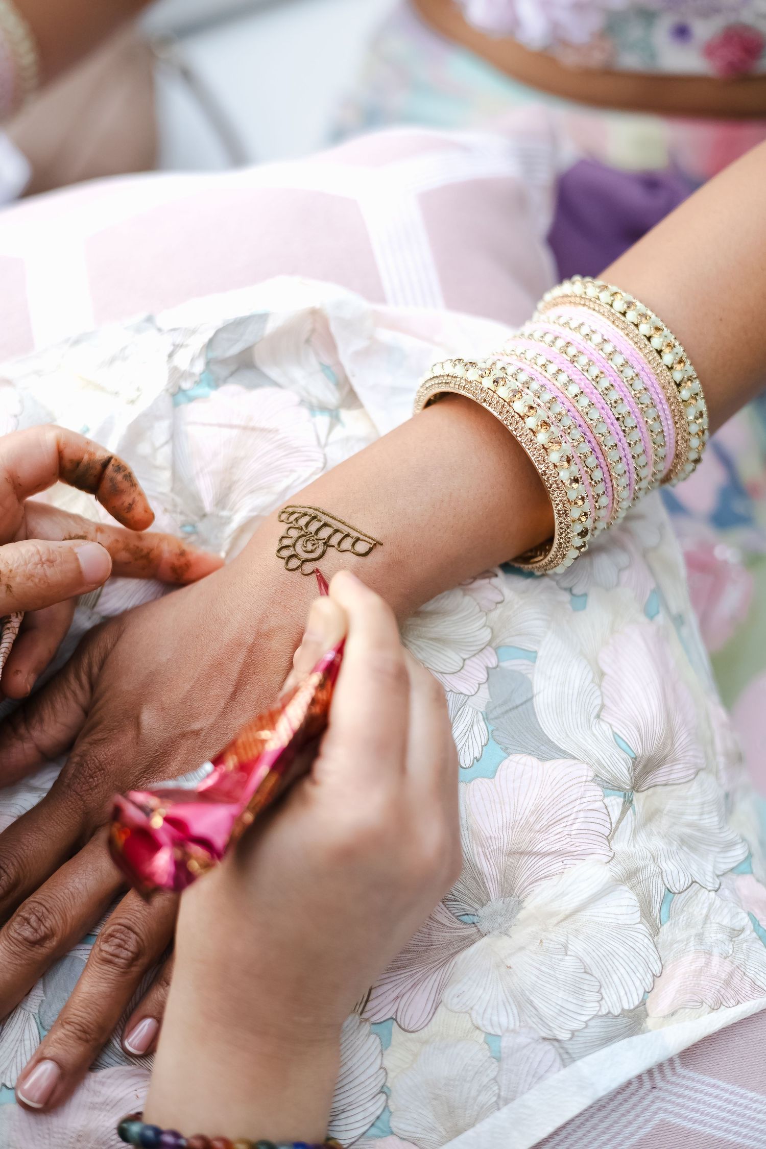 Hands adorned with delicate pearl bracelets placing decorative henna designs on wrists during a traditional ceremony.