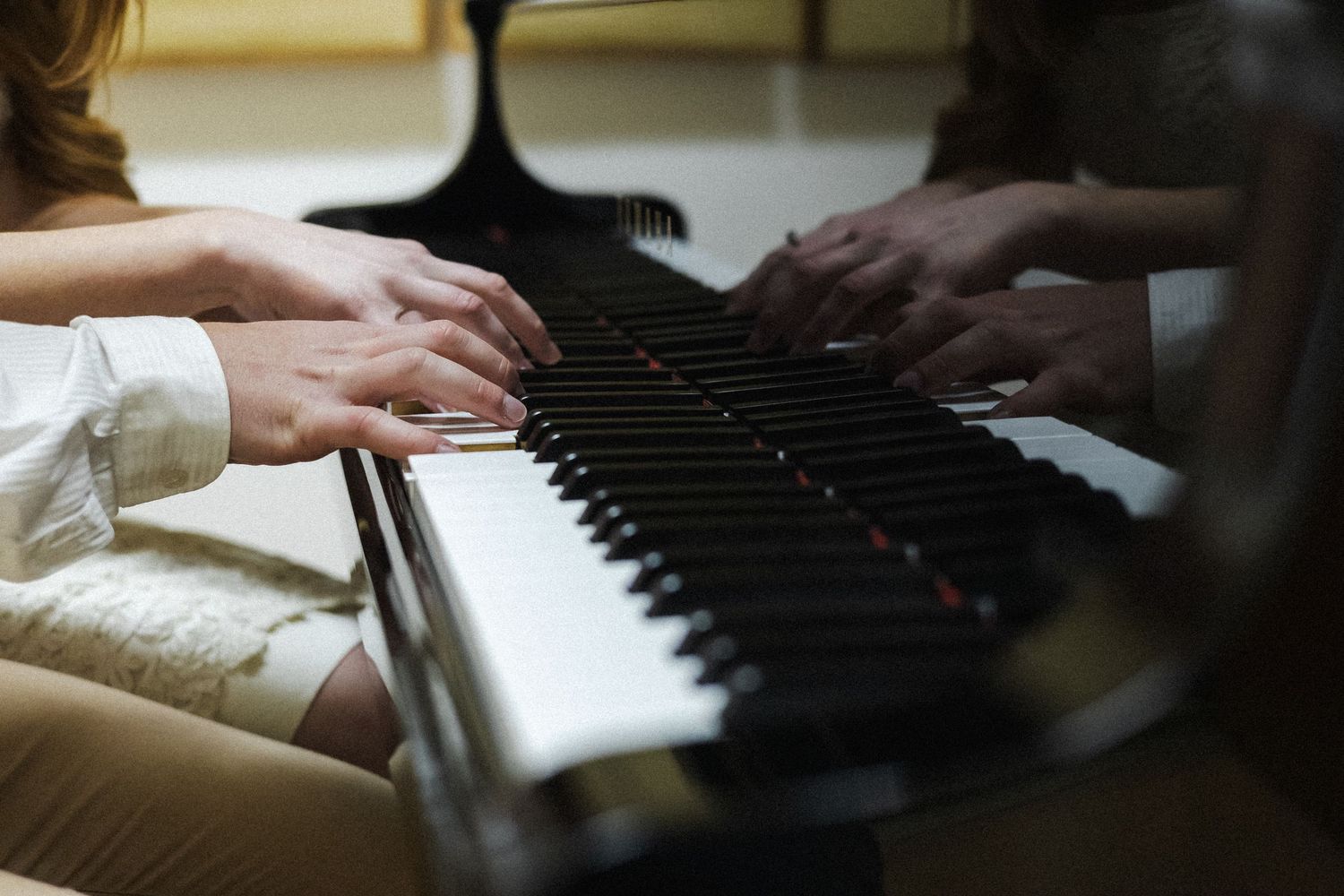 Hands playing on black and white piano keys in warm lighting with shallow depth of field.
