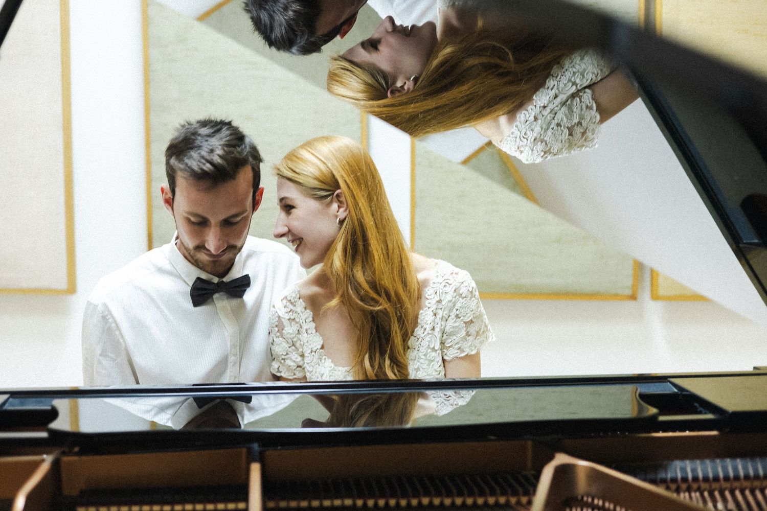 Two musicians collaborate while practicing at a piano in a rehearsal space.