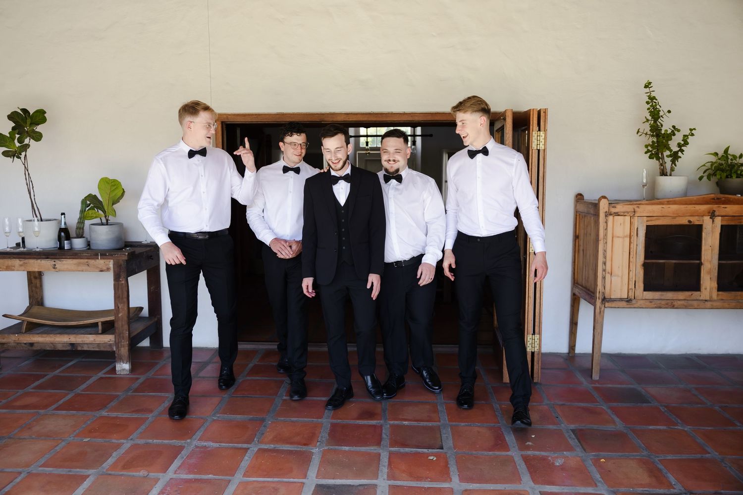 A group in formal black and white attire poses together on terra cotta tiles outside.