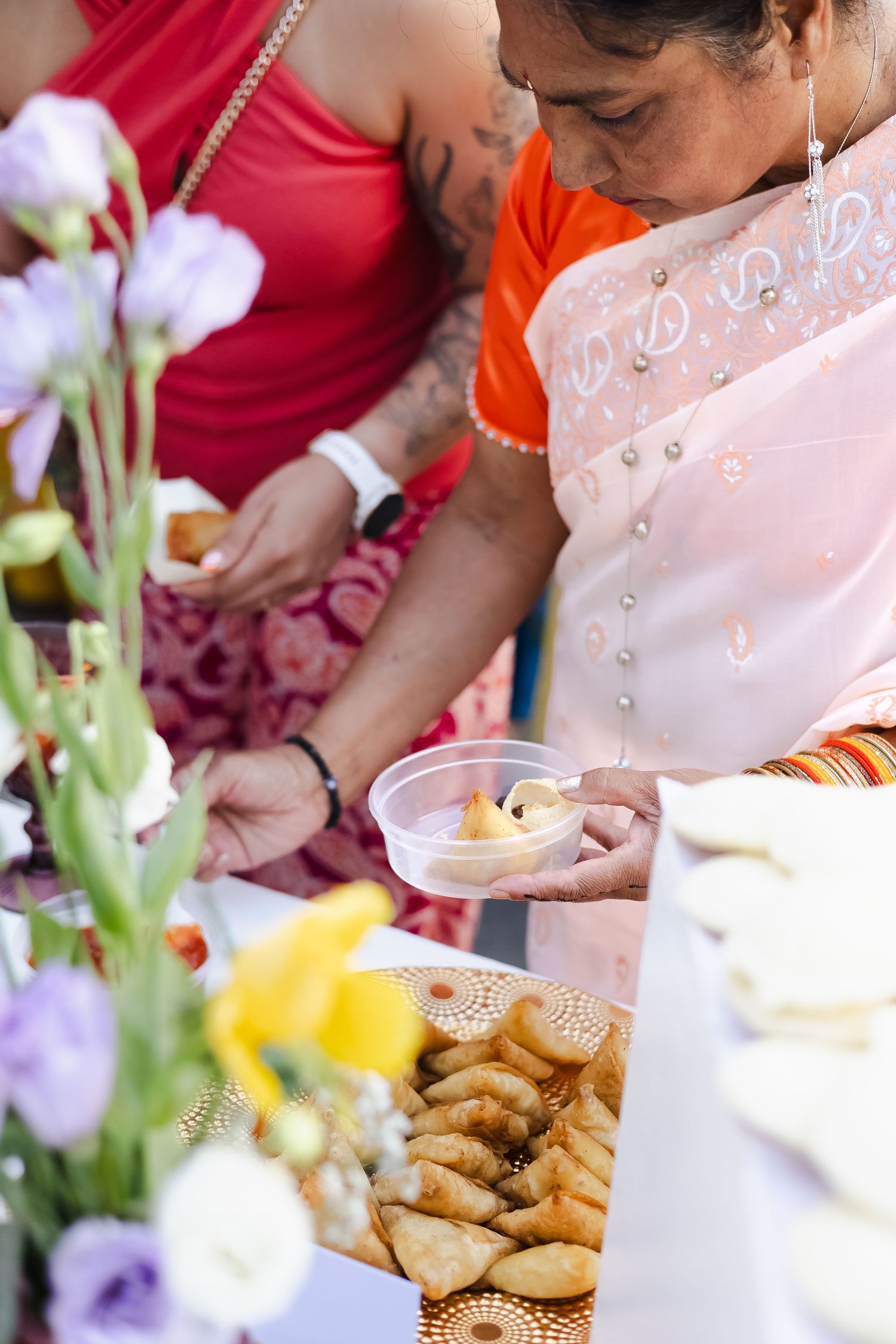 Close-up of hands serving traditional food at an outdoor gathering with flowers in the background.