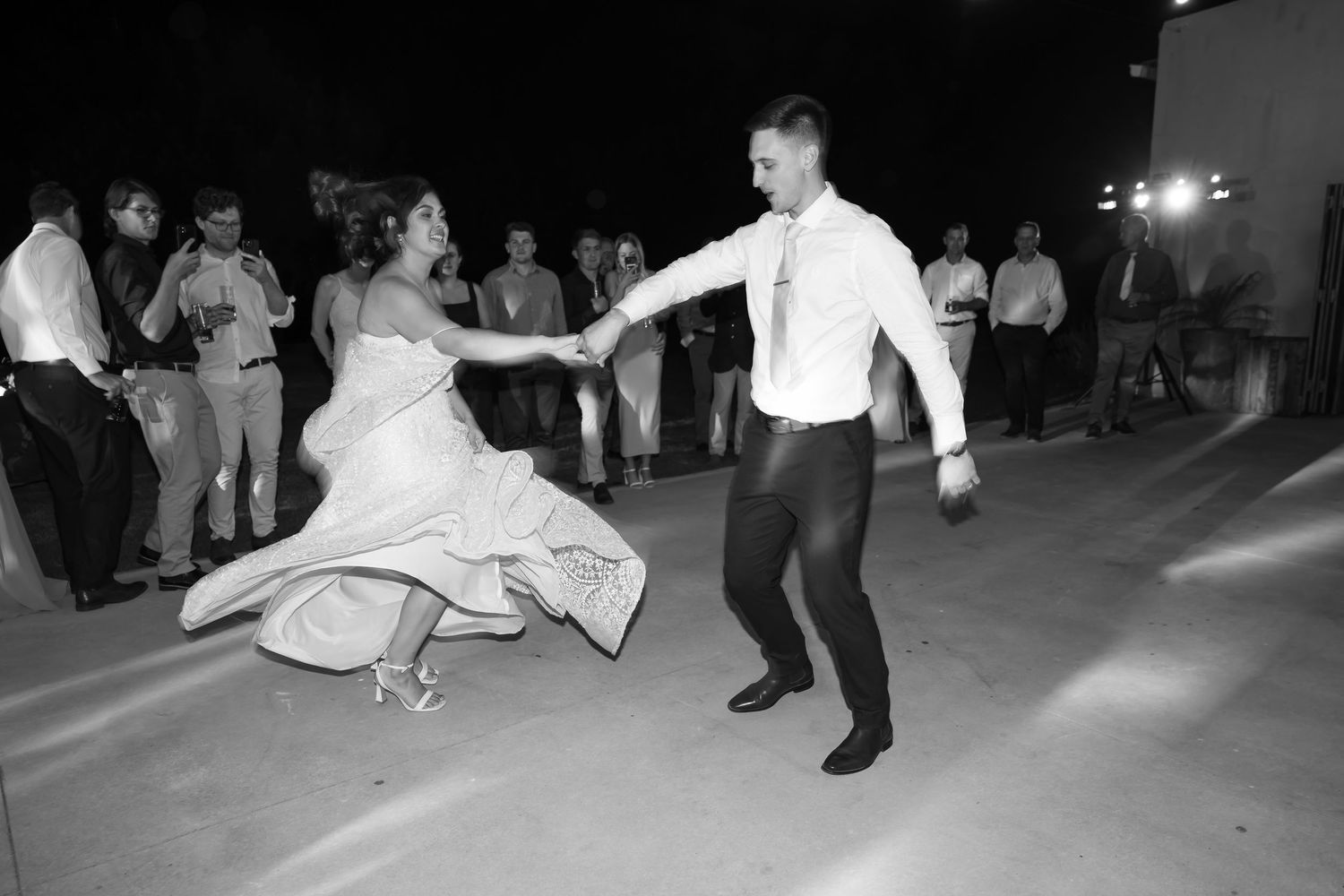 A couple dances together at a wedding reception, with the bride's white dress swirling on the dance floor.