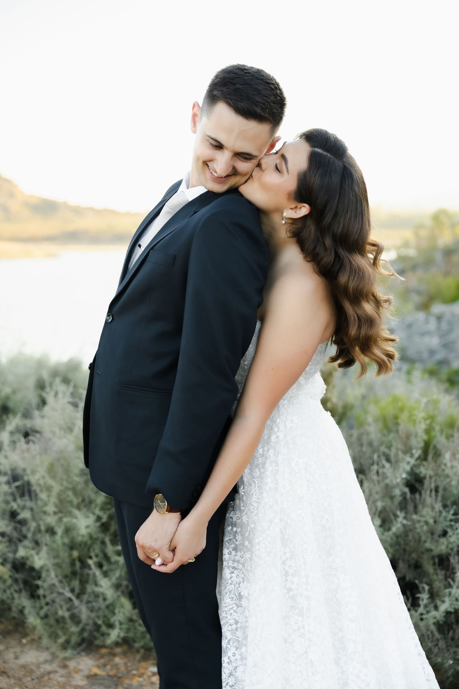 A romantic wedding couple shares an intimate moment outdoors with desert brush and natural scenery in the background.