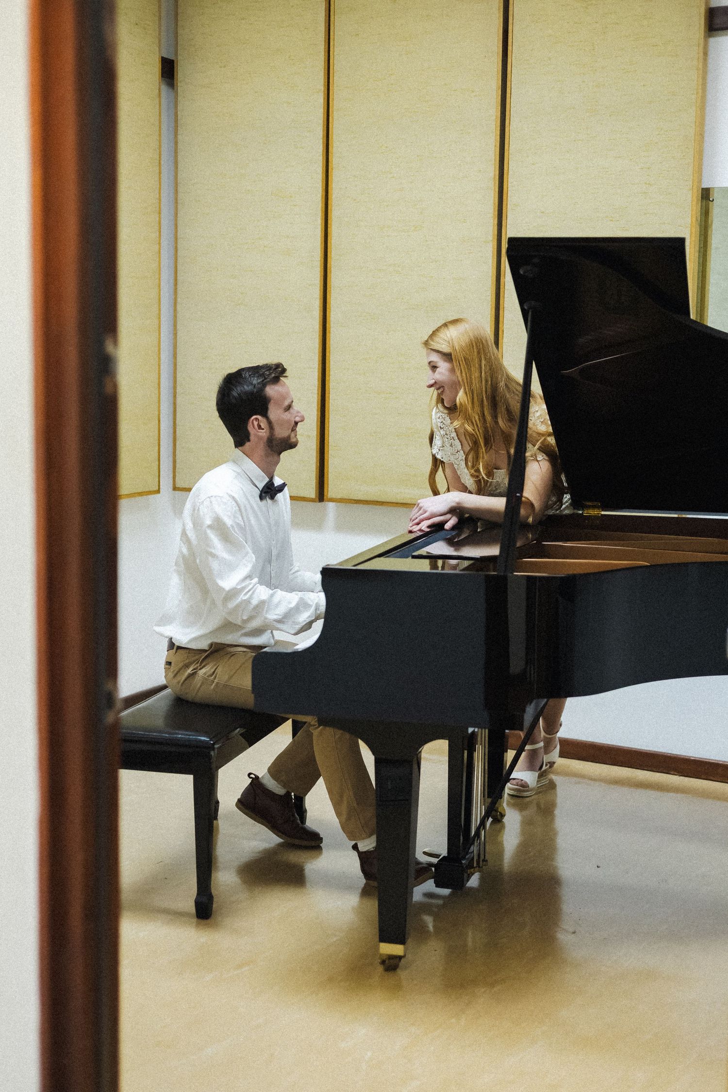 Two musicians rehearse together at a grand piano in a practice room.