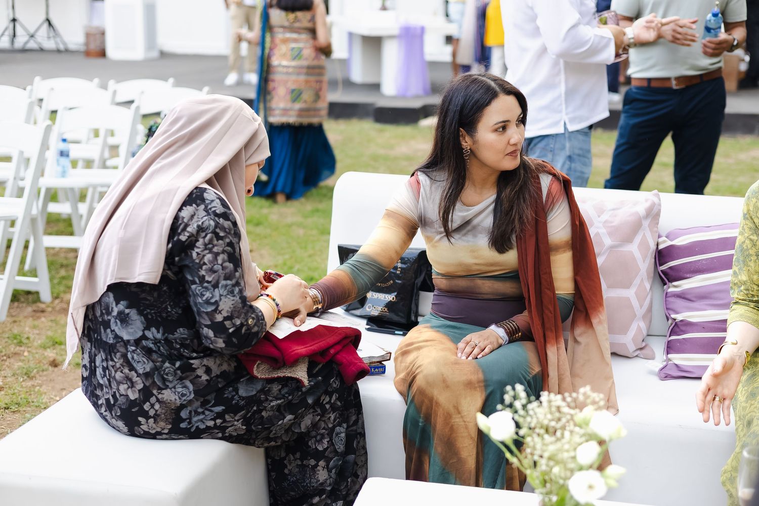 A group gathers around an outdoor table at a garden party with decorative floral arrangements and refreshments.