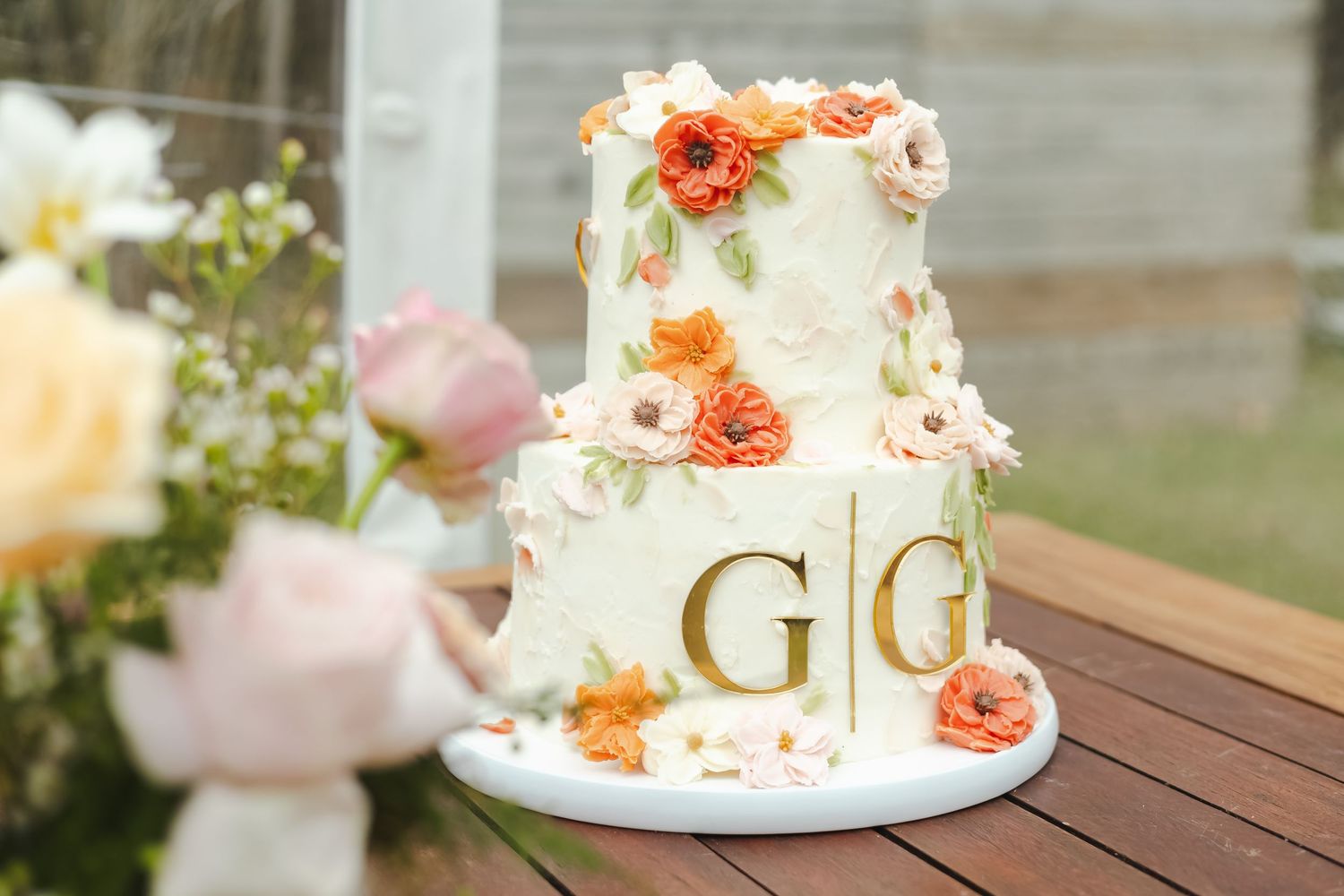 Wedding cake decorated with peach and coral flowers displayed on a wooden table.
