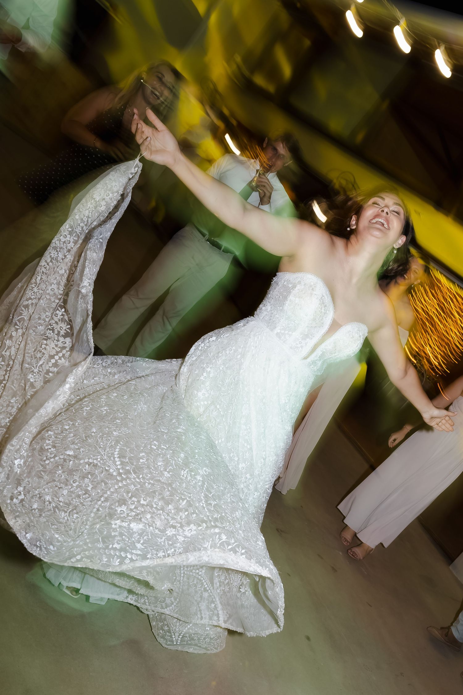 A bride in a white sequined wedding dress spins and dances joyfully on the dance floor during a reception celebration.