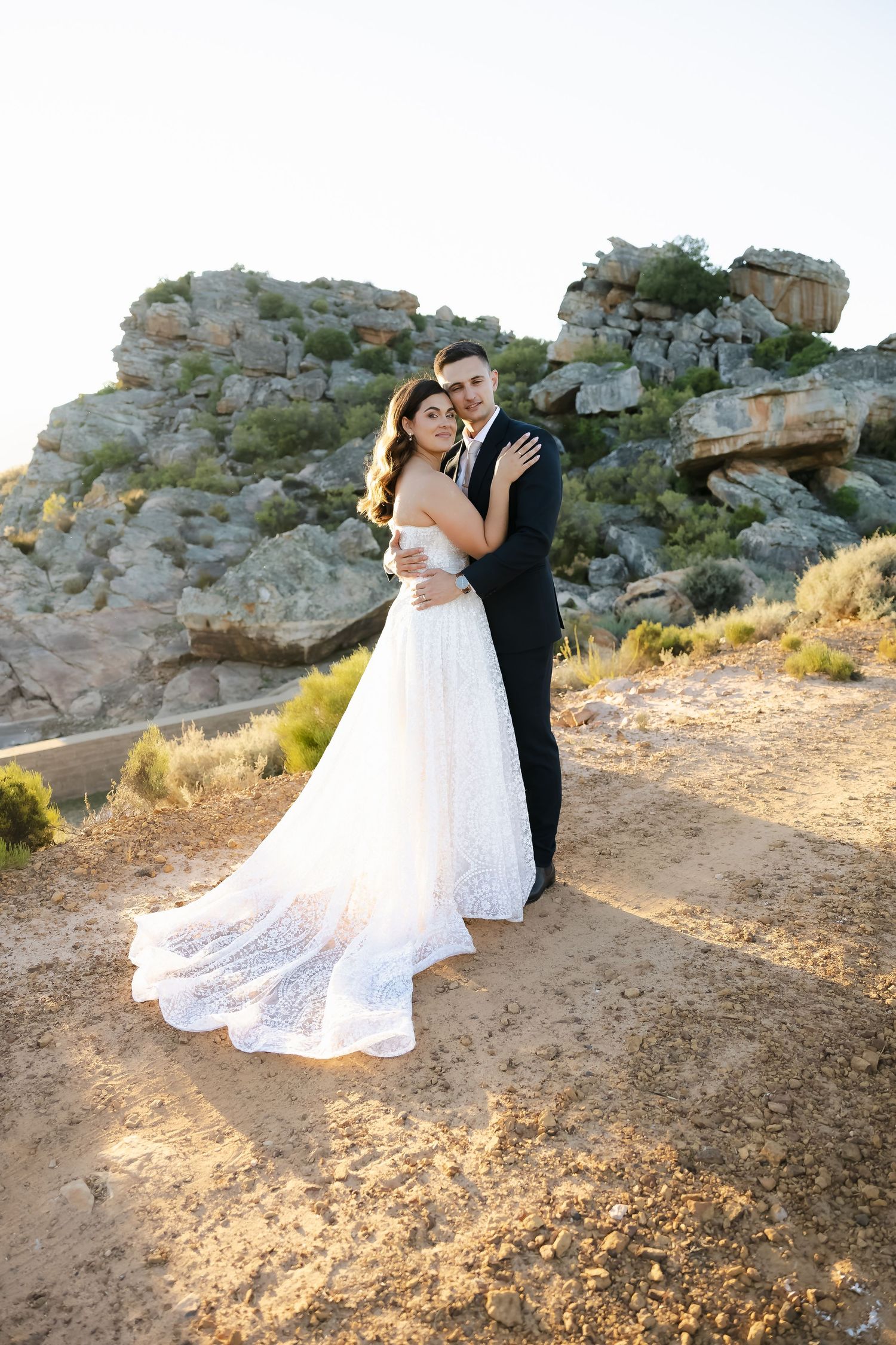 Wedding couple poses dramatically on rocky terrain during golden hour photography session.