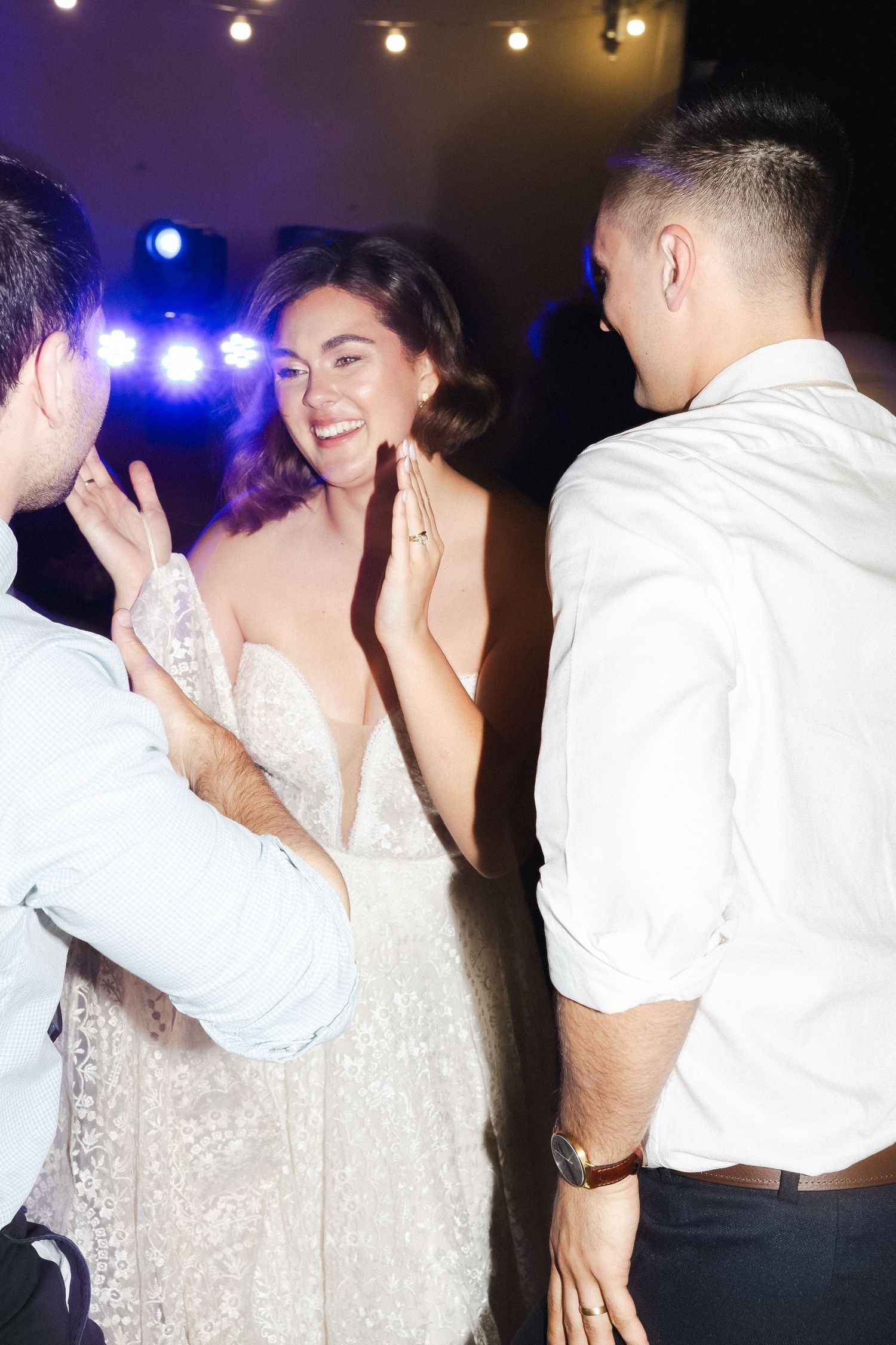 Wedding party dancing and celebrating at a reception with string lights and festive atmosphere.