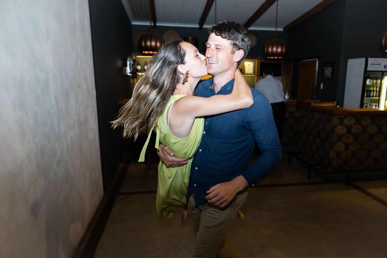 Wedding guests dancing and embracing on dimly lit dance floor during evening reception.