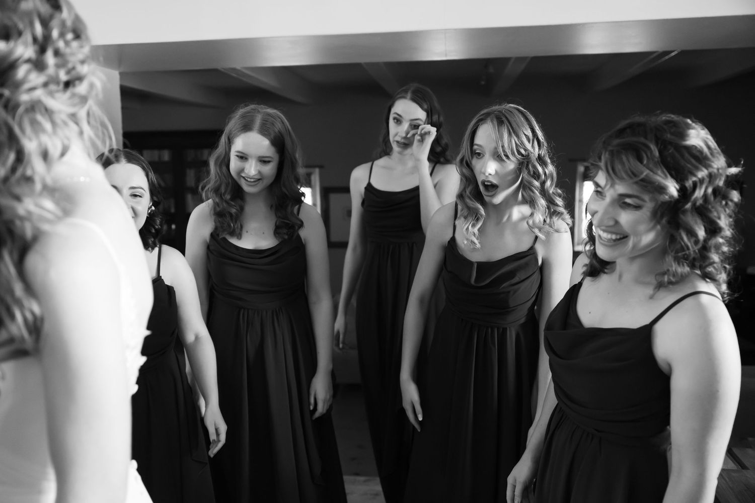 A group in black dresses stands together in a dimly lit room creating an elegant silhouette.