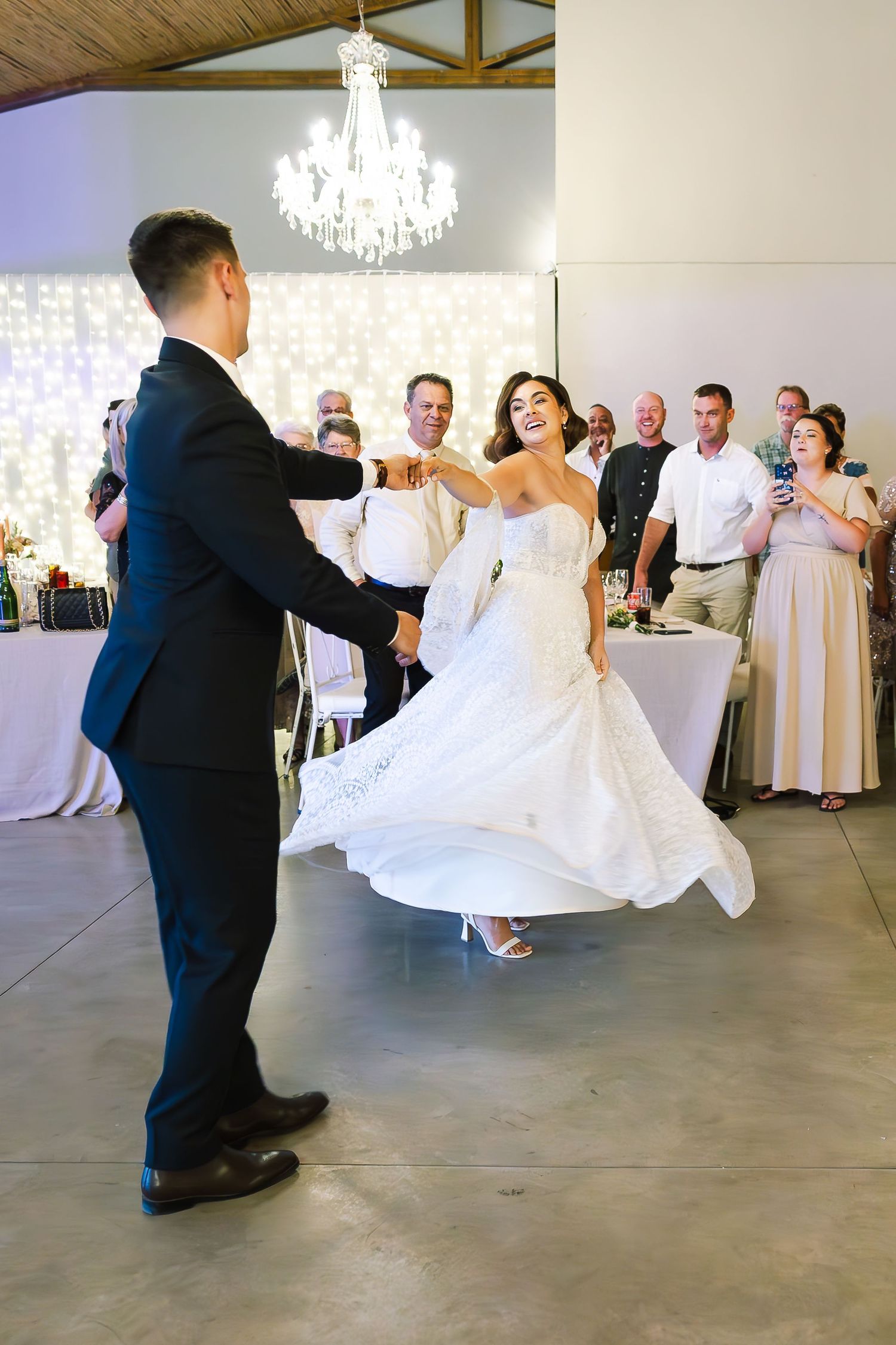 A couple shares their first dance at a wedding reception under an elegant crystal chandelier in a modern venue.