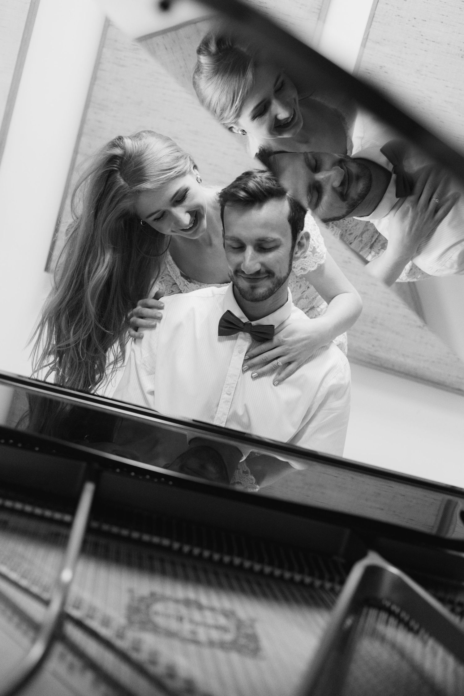 A couple shares an intimate moment while seated together at a piano in black and white photography.