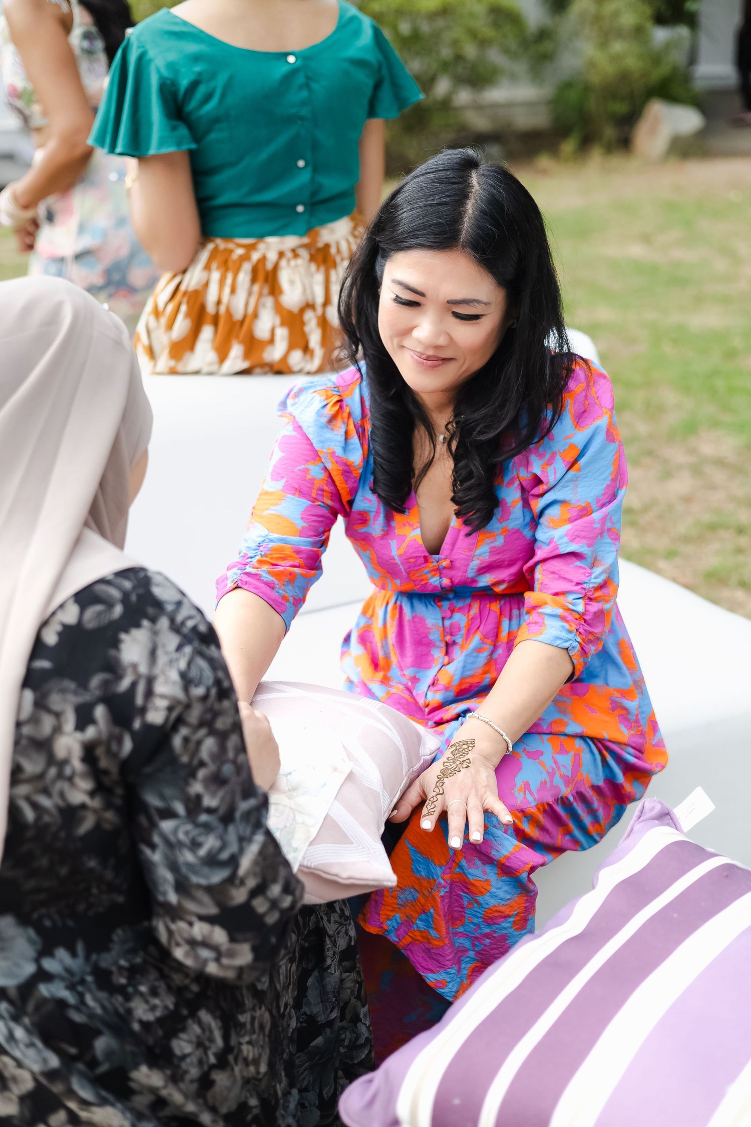 Someone in a vibrant pink and blue floral dress sits outdoors while opening a gift at a gathering.