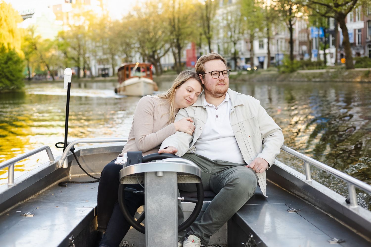 Couple relaxing on a boat cruise along an Amsterdam canal surrounded by autumn trees and historic buildings.